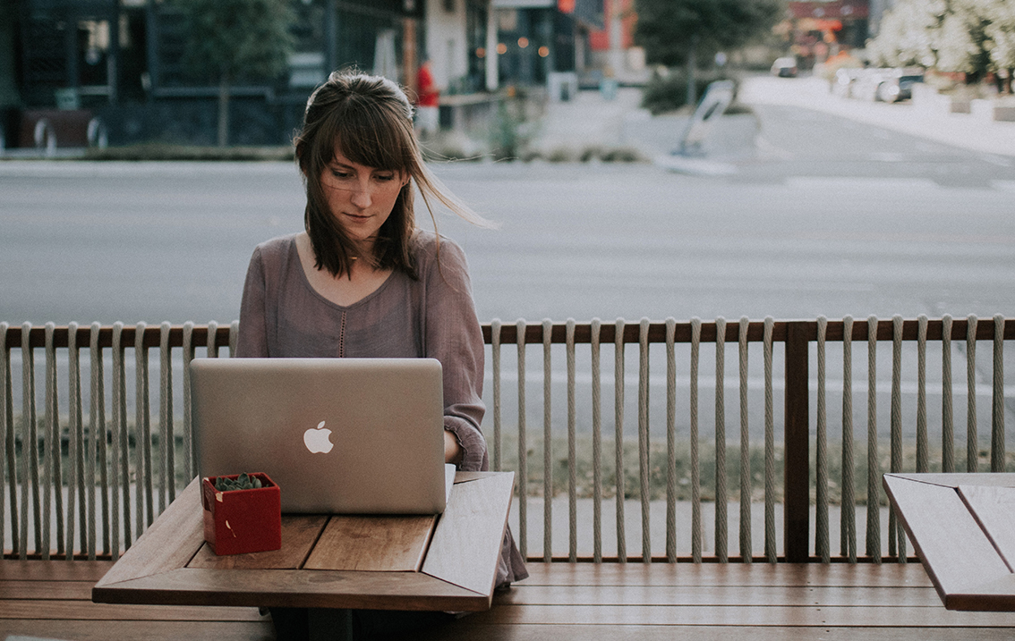 A woman using her laptop at an outdoor cafe on the street.